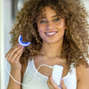 Woman holding Diamond Smile Power+ phone-bleaching mouthpiece with LED tray