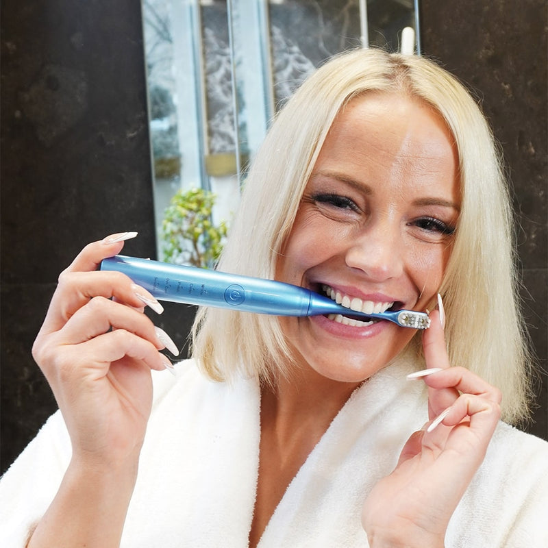 Woman with Power LED bleaching sonic toothbrush from Diamond Smile in her mouth in the bathroom